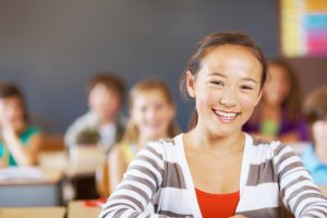 Portrait of cheerful girl sitting in classroom while classmates in background